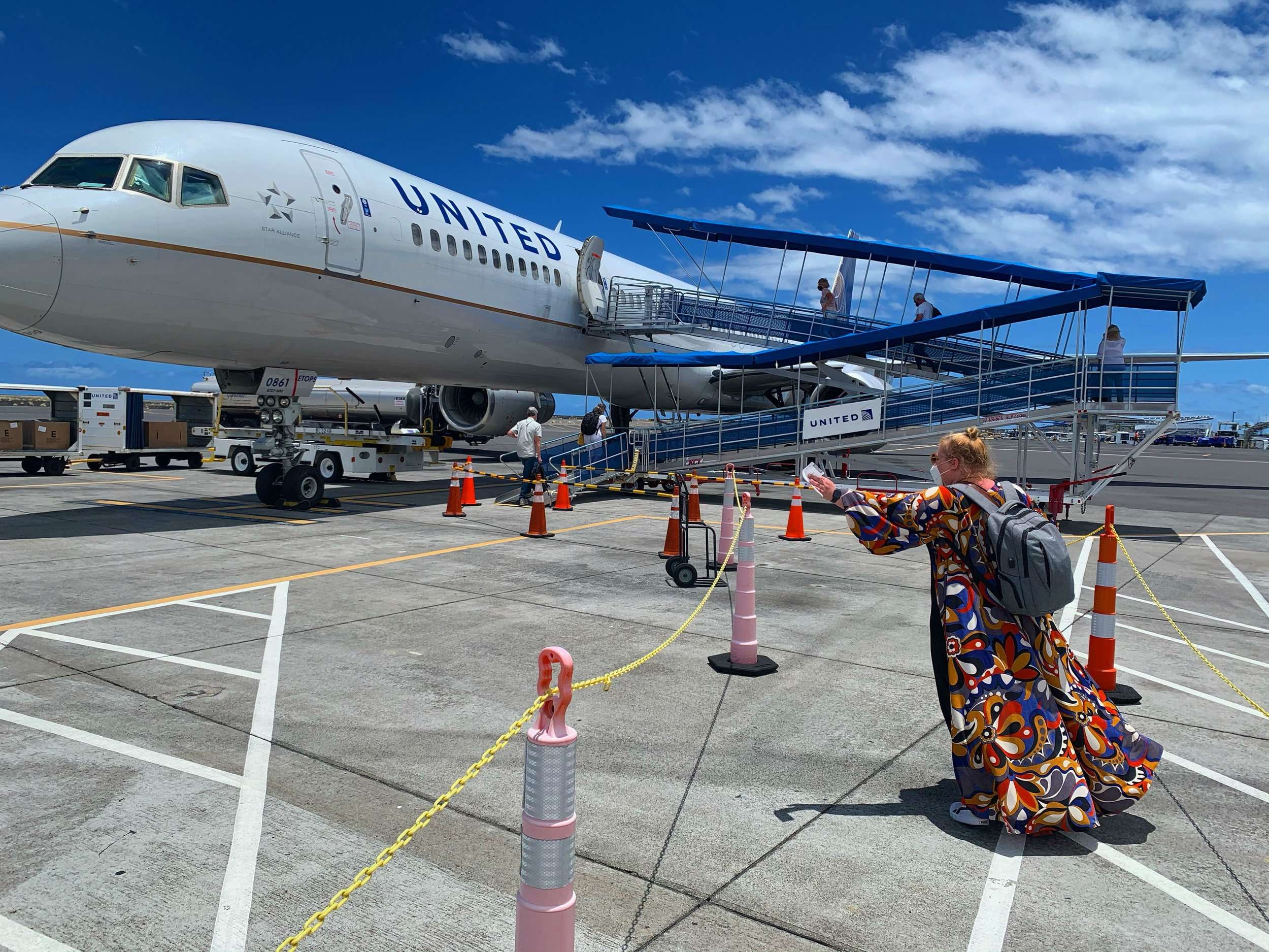 A blonde woman in a colorful duster boards a United plane outside